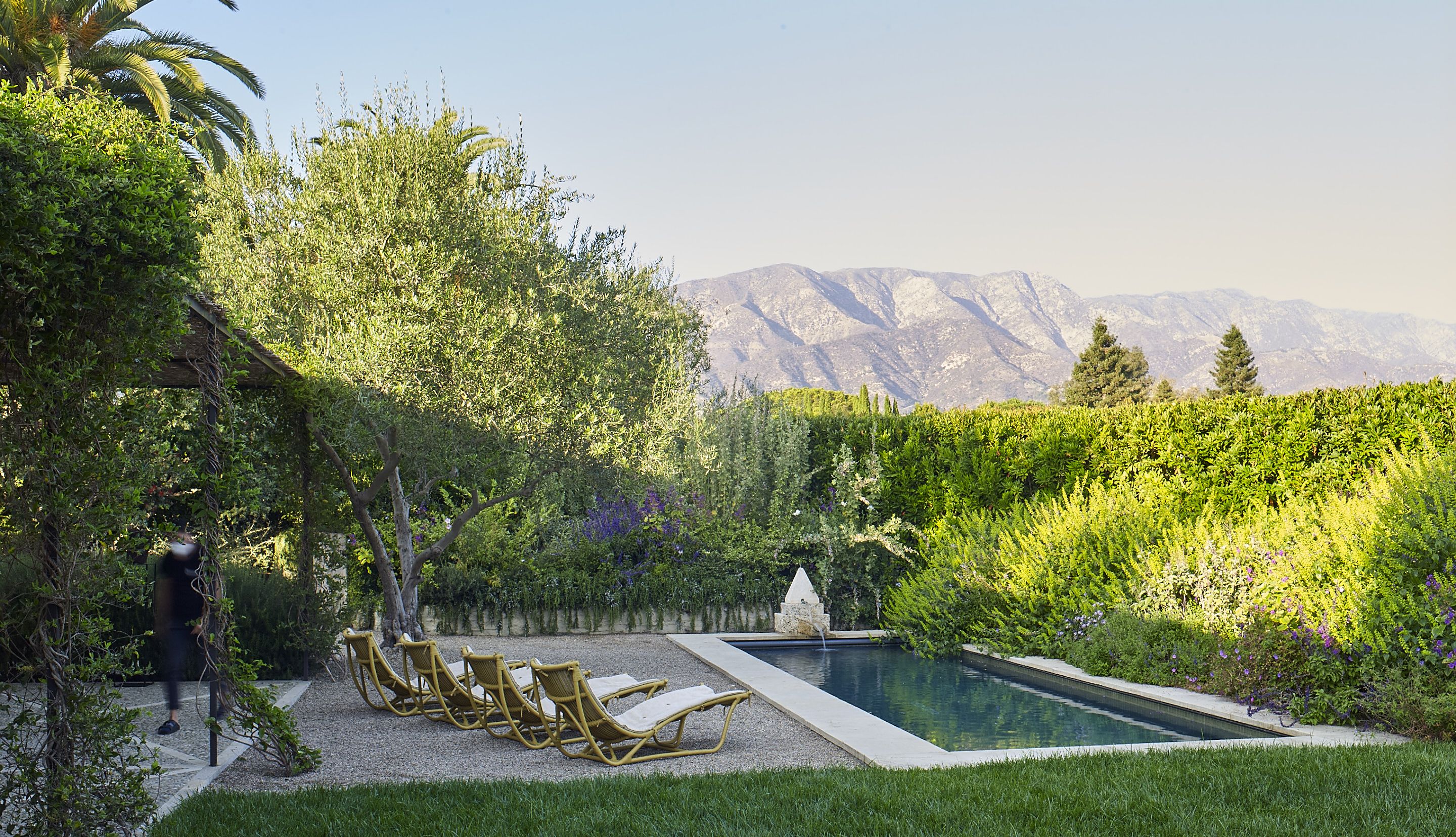 A serene backyard with a lap pool and 4 chaise lounges, surrounded by lush landscaping, and with moutains in the background